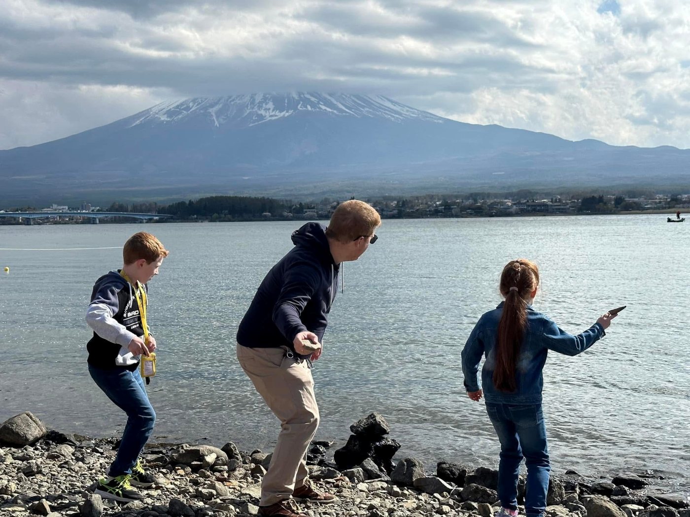 Three of the Watt family skimming stones from a rocky shore across a wide lake, a snow-topped mountain in the distance.